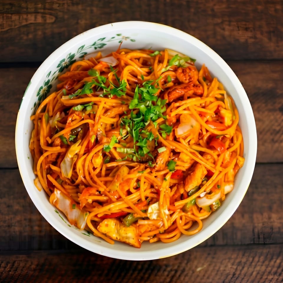 A white bowl filled with orange noodles, chicken, vegetables, and garnished with fresh green herbs.